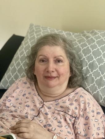 Carm, in a pink pajama top, sitting up in bed, with a grin on her face.